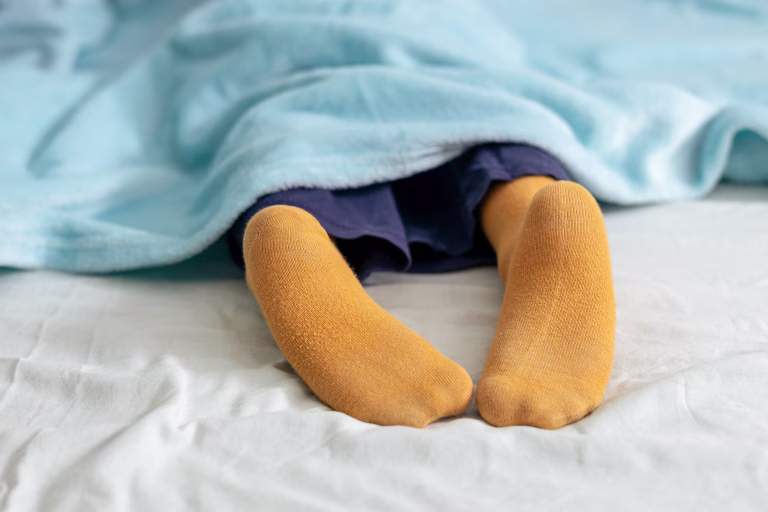 Child sleeps soundly under a blue blanket, an yellow sock peeking out, evoking a sense of peaceful rest