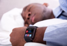 Šport porablja utripe srca in ti krajša življenje: MIT ali RESNICA? Close-up Of A Man Sleeping With Smart Watch In His Hand Showing Heartbeat Rate