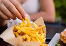 Pri nastanku diabetesa ima veliko vlogo TA prigrizek Closeup of young womans hand grabbing a crispy golden fries. Enjoying potato chips with a juicy burger in fast food restaurant on summer day. Selective focus