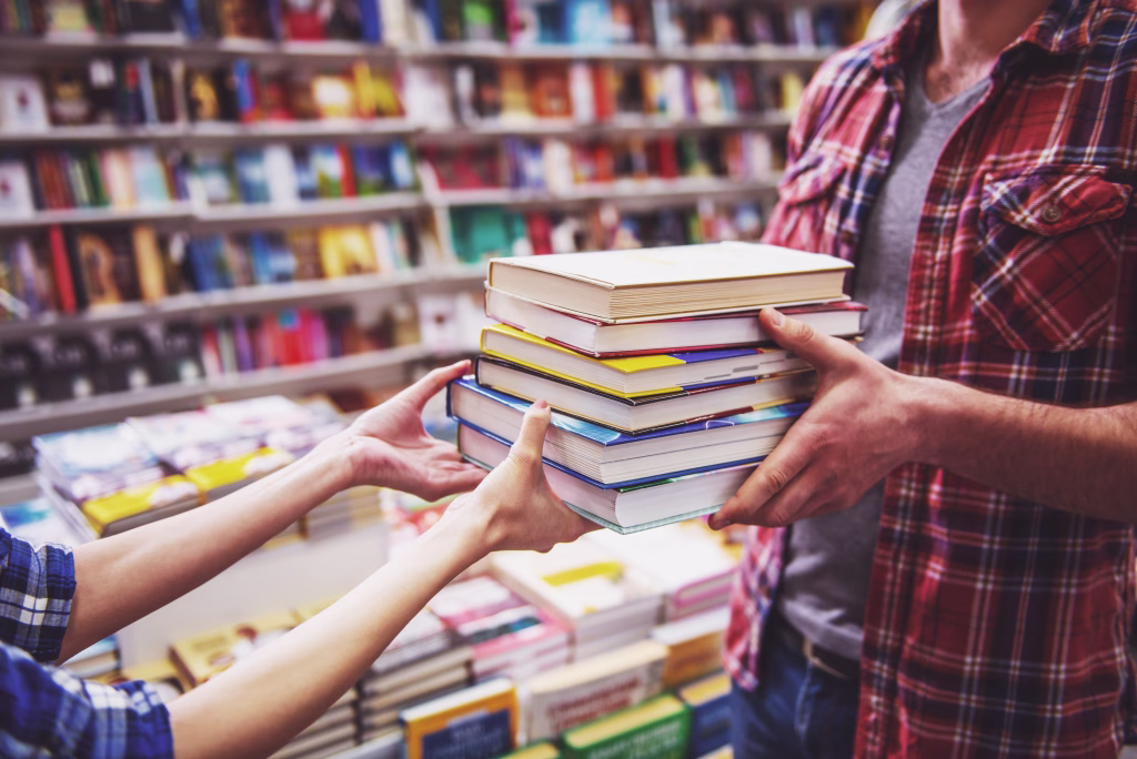 Cropped image of young man and woman holding a pile of books while standing in the book shop
