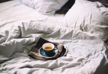 Kako kava vpliva na spanje? Drži, da zaradi nje spimo slabše? Delicious fresh morning espresso coffee in bed in a ceramic blue cup with a saucer, on the metal tray and black kitchen cloth, morning mood