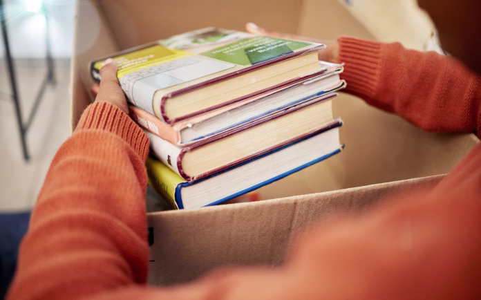 donation-charity-and-woman-hands-with-books-in-box-for-nonprofit-and-cardboard-container-at-home-education-textbook-donating-and-house-with-giveaway-and-spring-cleaning-for-community-support-stockpack-istock Donation, charity and woman hands with books in box for nonprofit and cardboard container at home. Education textbook, donating and house with giveaway and spring cleaning for community support