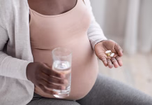 Ali sta tylenol in avtizem povezana? Prenatal Vitamins And Supplements. Unrecognizable black pregnant woman taking pills capsules and glass of water, using medicaments for healthy pregnancy, cropped image, closeup