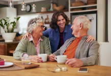 Ali so polnoletni dolžni skrbeti za svoje starše? Senior father and old mother sharing tea and heartfelt conversation with daughter at home at tea time. Elderly parents and beautiful daughter bonding over tea and discussion. Warm daughter embracing from behind her joyful parents while sitting at table and having a good conversation.