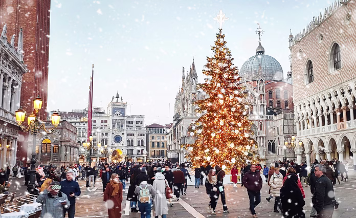 Venice, Italy - 25 December, 2023: People enjoying and walking in San Marco square in snowing Christmas evening in Venice. Christmas tree with decorations near Doge's Palace. Italy, Europa.