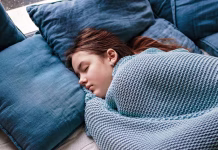 Razlog, ki potrjuje, da je spanje pozimi še posebej pomembno Young teenager girl sleeping snuggled in warm knitted blue blanket. Seasonal melancholy, apathy and winter blues. Cozy home.