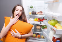 S preprosto spremembo v prehrani do 16 % boljšega spanca Young woman with pillow yawning standing in front of the refrigerator. Concept of eating during the night