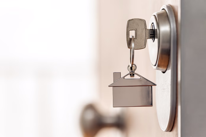 Close-up of house key and keychain inserted into a high security door lock. Real estate and home security concept. Copy space.