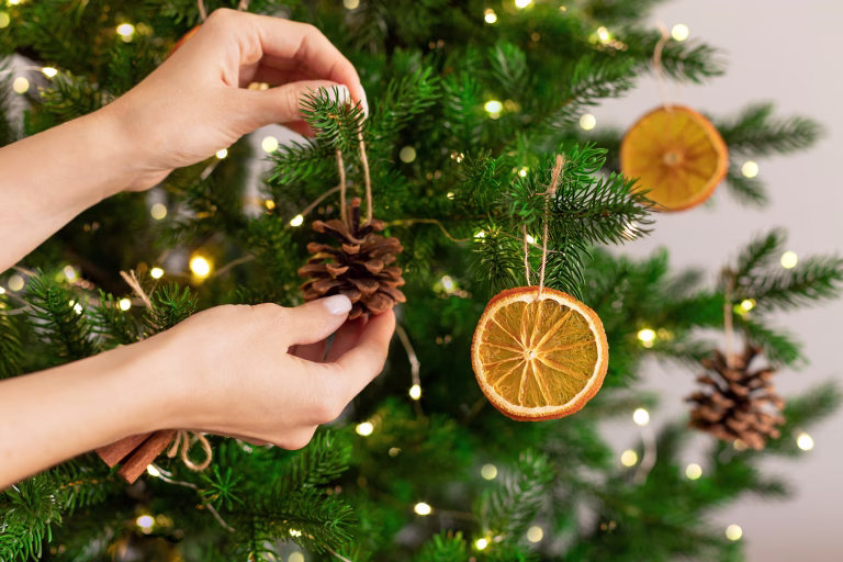 Female hands hanging handmade decoration on Christmas tree. Sustainable Christmas, zero waste, eco friendly.