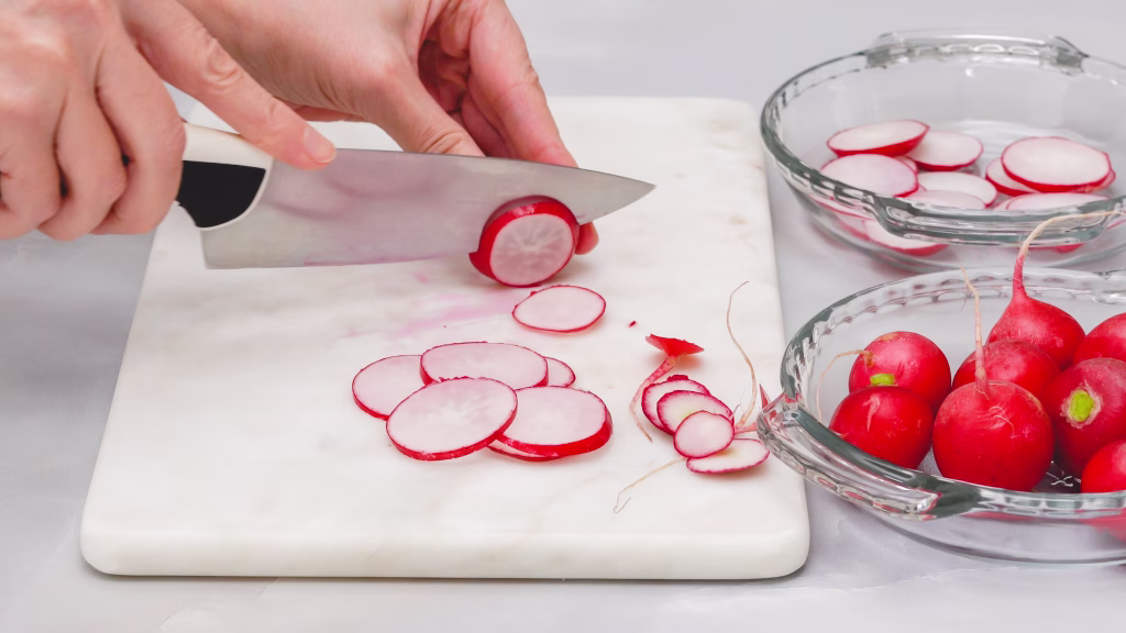 Fresh sliced radish close up on marble cutting board on light grey background. Vegetable salad preparation process, recipe