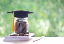 Davki za študente: kako je obdavčena štipendija? Graduation hat on coins money in the glass bottle on natural green background, Saving money for education concept