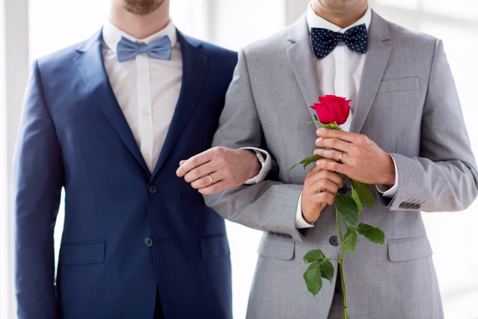people, homosexuality, same-sex marriage and love concept - close up of happy male gay couple with red rose flower holding hands on wedding