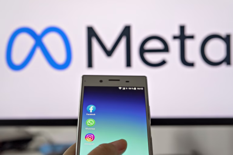 Smartphone display with logo of Facebook, WhatsApp and Instagram apps in hand against blurred META logotype on white monitor background: Tallinn, Estonia - October 29, 2021