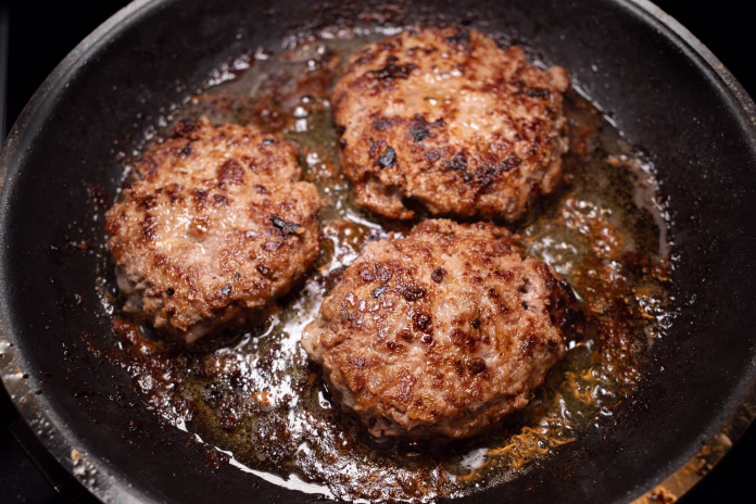 Three Swedish minced beef patties sizzle in golden butter, frying to perfection in a hot pan.