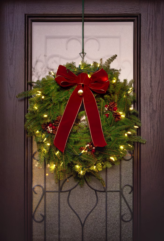 Traditional Balsam Fir Christmas wreath hanging on a front door. Red bow and holiday lights.
