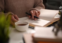 Najboljši čaji za določen čas dneva: kateri čaj je najbolje piti zjutraj in zvečer? A female reading a book or writing a diary and sipping hot tea in cozy home workspace. leisure and hobby concept