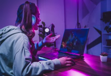 Najbolj zanimiv prenosni računalnik zadnjih let: kaj je prinesel začetek leta? A young woman enjoys streaming a live gaming session from her home, using a laptop and microphone setup under vibrant neon lighting.