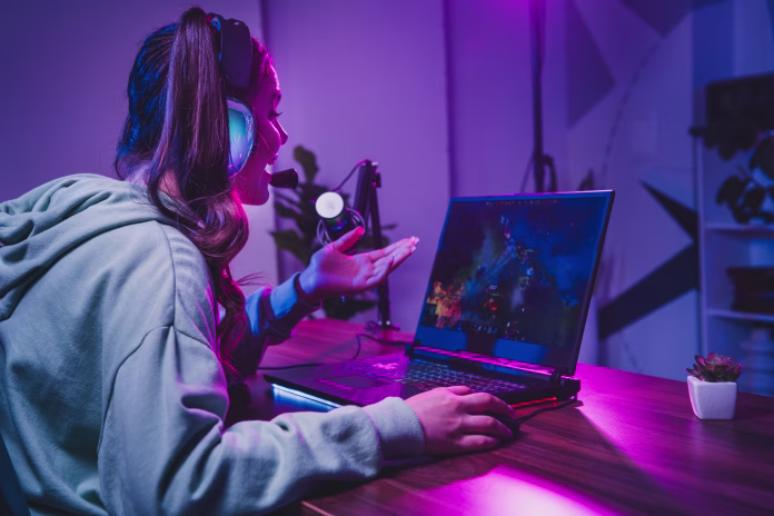 A young woman enjoys streaming a live gaming session from her home, using a laptop and microphone setup under vibrant neon lighting.