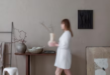 Hitra hrana, hitra moda in celo HITRO POHIŠTVO? Zakaj in kako izbrati trajnostno notranjo ureditev Aesthetic composition of warm living room interior with mock up poster frame, woman with vase, wooden consola, gray bowl, black ladder, beige wall and personal accessories. Home decor. Template.