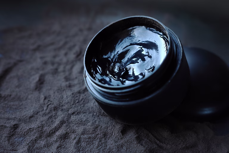 Black jar with black gel on black powder. Facial care products.