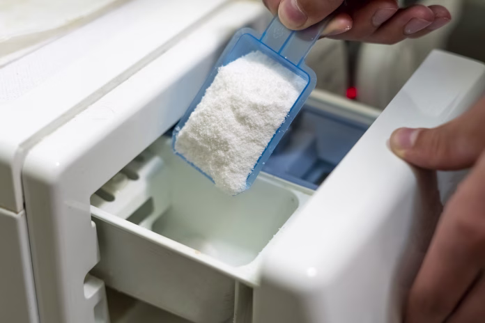 close up female hand pour the washing powder detergent into machine