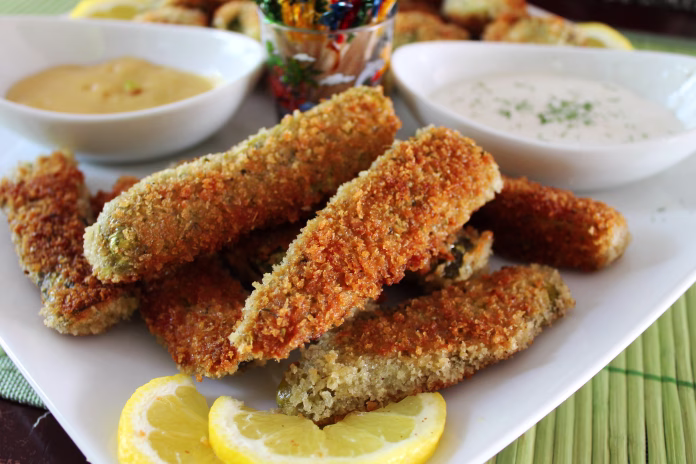Deep fried dill pickles, with dipping sauce, and sour cream and chives. White plate and bowls, colorful toothpicks.
