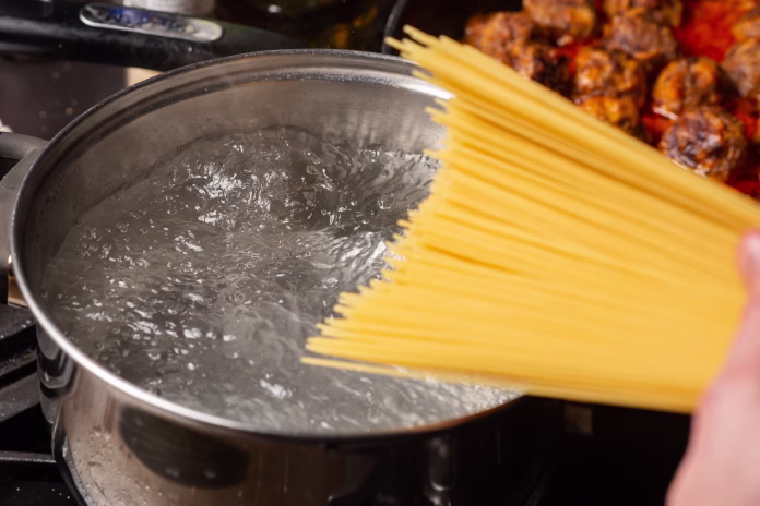 Dip spaghetti into boiling water in a saucepan. Pasta cooking.