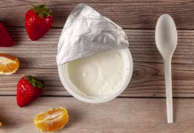 Bizaren recept, ki ga morate preizkusiti v letu 2026 Flat lay image of a store bought plastic cup of plain low fat Greek Yogurt with the aluminum foil seal peeled off. It is on wooden background with a plastic spoon and fresh fruits. A diet idea concept