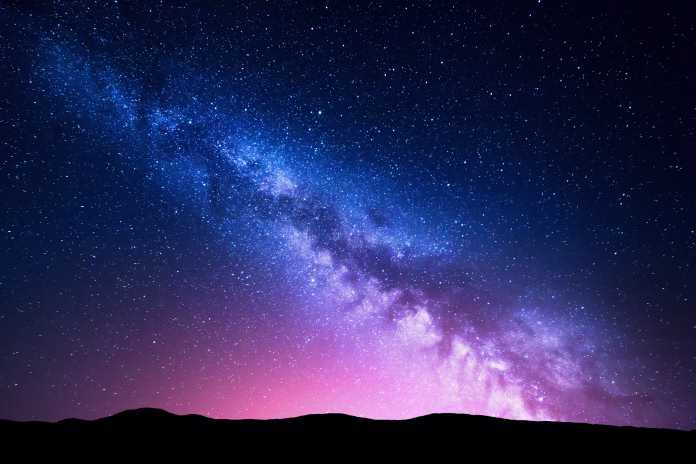 Milky Way and pink light at mountains. Night colorful landscape. Starry sky with hills at summer. Beautiful Universe. Space background with galaxy. Travel background