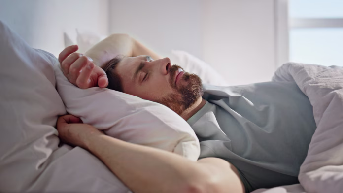 Sleeping man lying bed at morning closeup. Serene guy dreaming enjoying weekend at home interior. Handsome peaceful brunette resting comfortable pillow ignoring alarm. Lazy holiday lifestyle concept