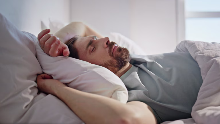 Sleeping man lying bed at morning closeup. Serene guy dreaming enjoying weekend at home interior. Handsome peaceful brunette resting comfortable pillow ignoring alarm. Lazy holiday lifestyle concept