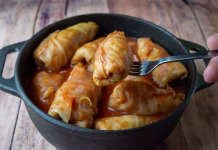 Vpliva praznična klasika na vitko postavo: koliko kalorij v resnici vsebuje sarma?! Stuffed cabbage rolls cooked in tomato sauce and served from a cast iron pot with a fork. Close-up view of a traditional homemade Eastern European cabbage dish on a rustic wooden table