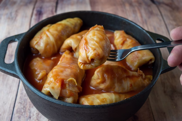 Stuffed cabbage rolls cooked in tomato sauce and served from a cast iron pot with a fork. Close-up view of a traditional homemade Eastern European cabbage dish on a rustic wooden table