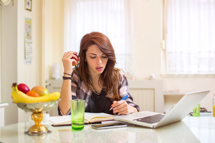 Teenage girl studying using books and laptop at home.
