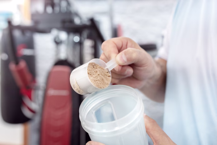 Whey protein powder in scoop and shaker bottle, man training and preparing protein shake drink in gym