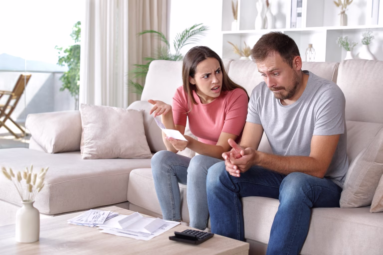 Wife scolding husband checking expenses sitting on a couch at home