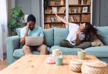 Nov cimer: kaj storiti, če dobiš neprijetnega sostanovalca? Young woman having fun and trying to distract her boyfriend working from home online on laptop. Freelance man work on a computer remotely via the Internet and his girlfriend is acting crazy and funny