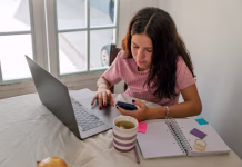 Multitasking med učenjem: dobra ideja ali napaka? Young woman sitting at a table with a laptop, smartphone, and notebook, studying or working remotely from home