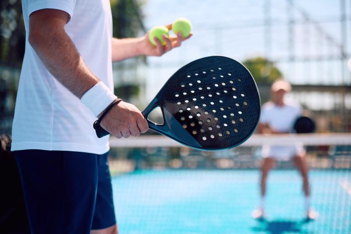Close up of athlete serving the ball while playing paddle tennis.