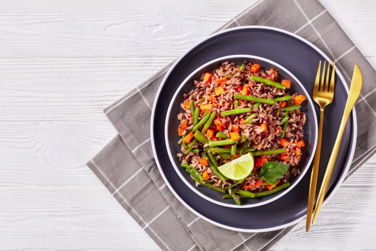 fried brown and wild rice with green beans and carrot on a plate, flat lay, free space