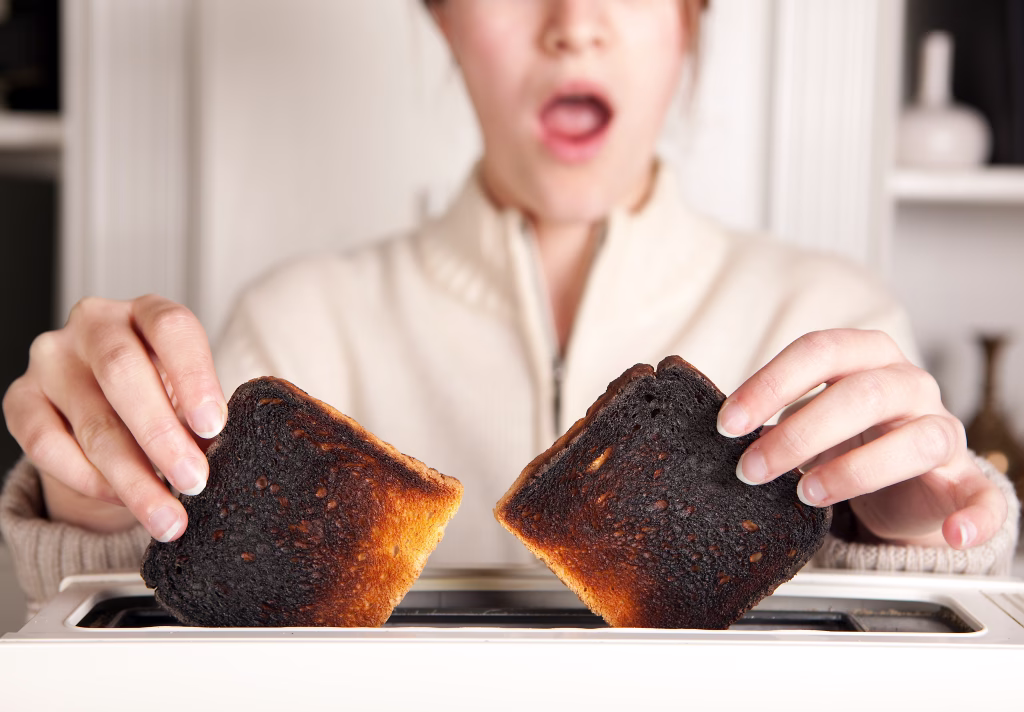 Hands of a woman taking burnt toast out of a toaster