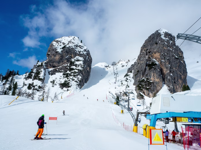 Olympic downhill ski run Olimpia 1 in Cortina dAmpezzo in Dolomites, Italy. The steepest part between big rocks. Ski lift and unrecognizable skiers. Slope often used for Alpine ski World Cup races