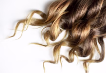 Zakaj je ta frizerska tehnika osvojila leto 2026? piece of brown curly shiny hair on white isolated background