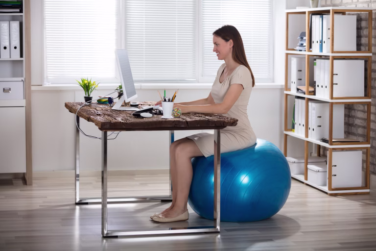 Smiling Young Businesswoman Sitting On Fitness Ball Using Computer