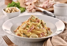 Študent kuha: Prava italijanska carbonara SPAGHETTI ALLA CARBONARA with mushroom and fork served in dish isolated on wooden table side view of italian fast food