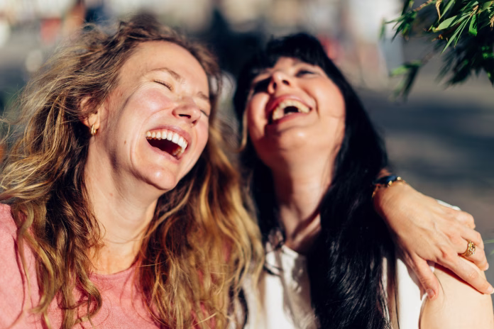 Two cheerful female friends are sharing a moment of joy and laughter, embracing each other outdoors in an urban setting