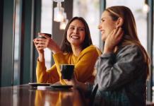 8 napak, ki jih vsak dan delate med pogovori (in se tega ne zavedate) Two female friends sitting at cafe having coffee and gossiping. Female friends meeting in a coffee shop on a weekend.
