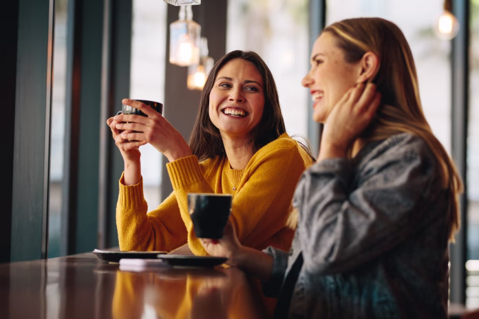 Two female friends sitting at cafe having coffee and gossiping. Female friends meeting in a coffee shop on a weekend.