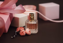 Parfumska ali toaletna voda? Razlika, ki jo je dobro poznati pred nakupom Women's Pink Perfume in Beautiful Bottle and Artificialt Flowers Bracelet on Brown Background with gift boxes.