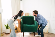 Najpogostejše napake pri prvi selitvi na svoje Young couple is carrying an armchair together while smiling and arranging furniture in their new home